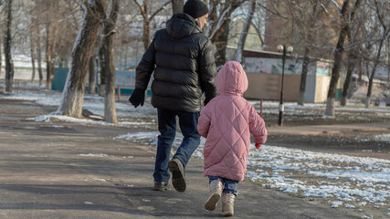 Grandfather playing with her granddaughter on the playground in the park in winter