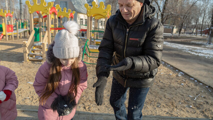 Grandfather playing with her granddaughters on the playground in the park in winter