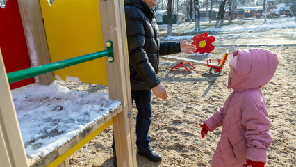 Grandfather playing with his granddaughter on the playground in the park in winter