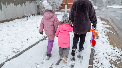 Grandmother and girls walk along a snowy street in winter