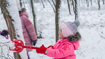Two little girls in colorful clothes play outdoors during a snowfall.
