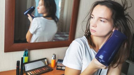 Young woman using a blow dryer and drying her hair in bedroom at home