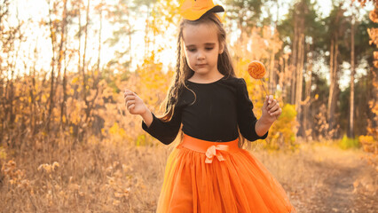 Portrait of a cute girl in a black witch costume asking for candy on Halloween eve. The child...