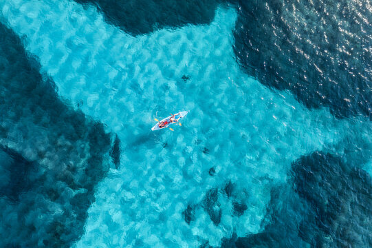Aerial view of a kayaker paddling through vibrant turquoise shallow waters surrounded by deep blue ocean, creating a breathtaking contrast and showcasing the beauty of a tropical paradise. Top view