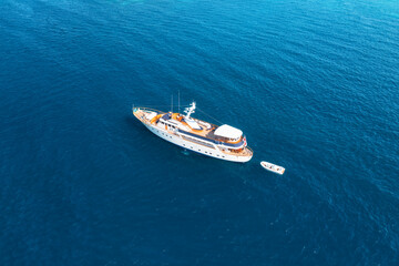 Aerial view of a luxurious yacht sailing on calm, deep blue ocean water, with a smaller tender boat nearby, offering a sense of tranquility and adventure