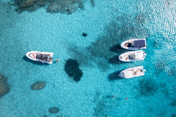 Aerial view of several motorboats floating on crystal-clear turquoise water in a beautiful tropical paradise cove, creating a serene and idyllic vacation scene