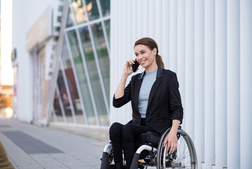 Smiling businesswoman in wheelchair using smart phone near office building