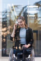 Smiling businesswoman in wheelchair using smart phone near office building
