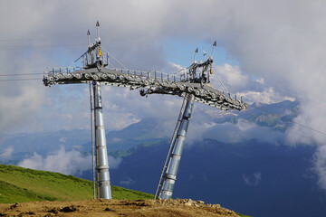  In a picturesque mountain setting, ski lift towers rise above lush green hills, framed by clouds...