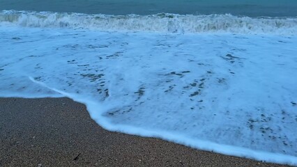 The soothing, tranquil ocean waves gracefully roll onto the sandy beach as dusk approaches
