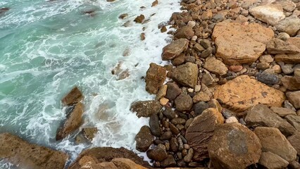 Experience mesmerizing waves crashing against the rocky shoreline, revealing turquoise waters