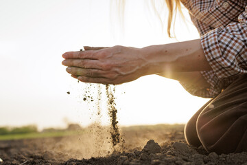 Hands examining dry soil on farmland at sunset, concept of agriculture and sustainability.