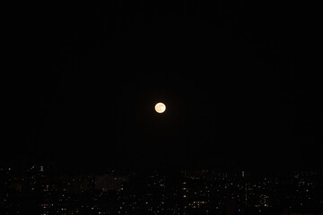 A bright full moon hangs in a clear night sky, casting a soft glow over the sprawling city below....