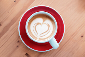 Top view of coffee cup with heart shaped latte art on red saucer and wooden table. Top view, flat lay