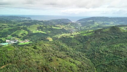 Obraz premium Aerial View Showcasing Lush Green Hills Gracefully Meeting the Vast Ocean Beyond