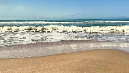 Enjoy the beautiful scene of serene beach waves gently rolling under a clear blue sky