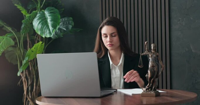 A young female lawyer is working on a laptop with a statue of Themis at her desk, preparing for a consultation. A notary is studying legal law. The concept of jurisprudence.