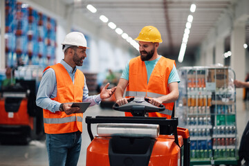 Warehouse workers discussing logistics while driving pallet truck and holding tablet