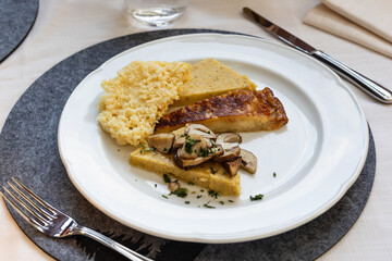 A beautifully plated serving of Frico and polenta, typical of Friuli Venezia Giulia, sits on a restaurant table with cutlery and a placemat, ready to be enjoyed.