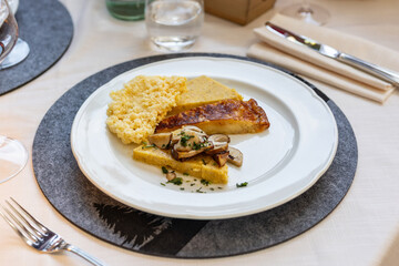 A beautifully plated serving of Frico and polenta, typical of Friuli Venezia Giulia, sits on a restaurant table with cutlery and a placemat, ready to be enjoyed.