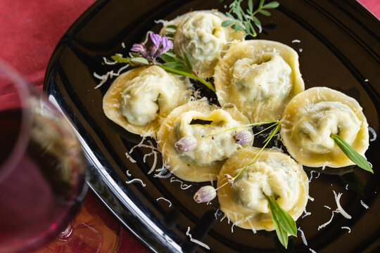 A white plate features beautifully arranged Cjarsons, a traditional pasta dish from Carnia in Friuli Venezia Giulia, garnished with grated cheese and spices.