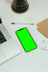 A green phone sits on a table next to a laptop