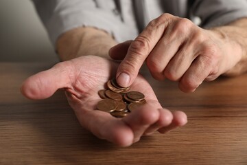 Senior man counting coins at wooden table, closeup. Financial problems