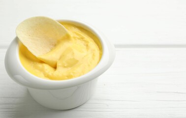 Tasty dipping cheese sauce in bowl and potato chip on white wooden table, closeup. Space for text