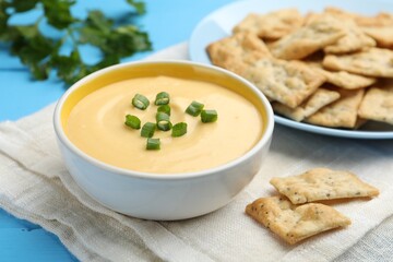 Tasty cheese dipping sauce in bowl and crackers on light blue table, closeup