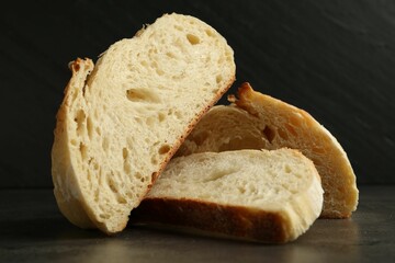 Slices of fresh bread on dark textured table against black background, closeup