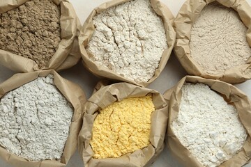 Different types of flour in paper bags on white table, flat lay