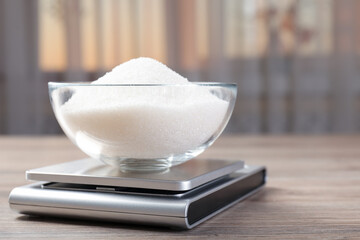Digital kitchen scale with bowl of sugar on wooden table indoors, closeup. Space for text