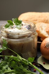 Pieces of delicious herring with spices and parsley in jar on black table, closeup