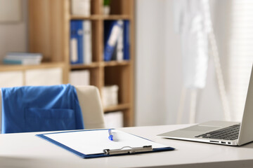 Doctor's workplace. Clipboard, pen and laptop on white table in medical office, closeup