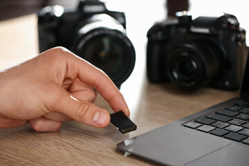 Man inserting SD memory card into laptop at wooden table indoors, closeup