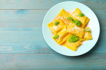 Delicious ravioli with cheese and basil on light blue wooden table, top view. Space for text