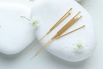 Acupuncture needles, pebble stones and flower buds on white table, flat lay
