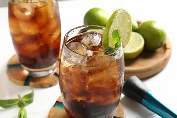 Tasty Cuba Libre cocktail in glasses, ingredients and muddler on white table, closeup