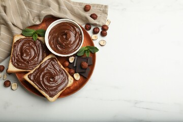 Toasts with chocolate hazelnut spread, nuts, pieces of chocolate and mint on white marble table, flat lay. Space for text