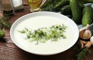 Tasty cucumber soup in bowl and ingredients on wooden table, closeup