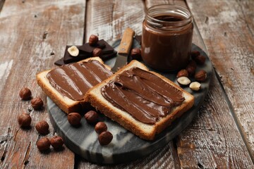 Toasts with tasty chocolate hazelnut spread and nuts on wooden table, closeup