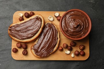 Toasts with tasty chocolate hazelnut spread and nuts on black table, top view