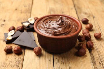 Tasty hazelnut spread, chocolate pieces and nuts on wooden table, closeup