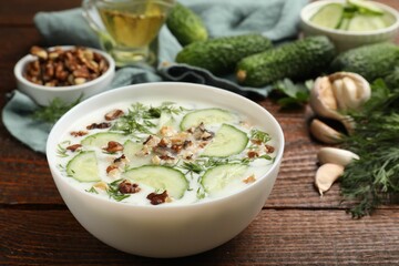 Tasty cucumber soup with dill and nuts in bowl on wooden table, closeup