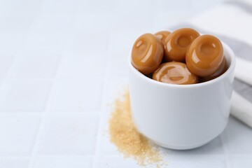 Tasty sweet caramel candies on white tiled table, closeup. Space for text