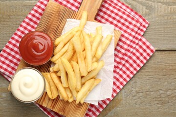 Tasty french fries with sauces on wooden table, top view