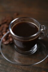 Aromatic coffee in glass cup and beans on wooden table, closeup
