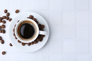 Aromatic coffee in cup and beans on white tiled table, flat lay. Space for text