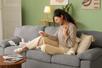 Young African-American woman sitting on sofa and suffering from skin allergy at home
