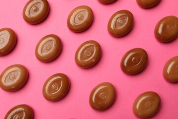 Many tasty caramel candies on pink background, flat lay